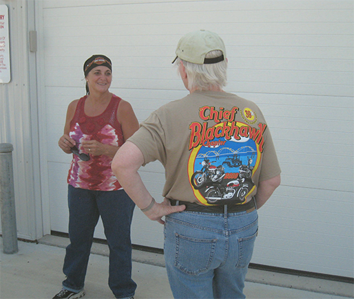 Picture of an older man wearing a Chief Blackhawk graphic T-shirt talking with a woman inside a building with white walls